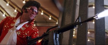 Movie still from “3000 Miles to Graceland” (2001), directed by Demian Lichtenstein – A man in a red shirt holding a gun; Medium shot, Low angle