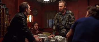 Movie still from “3000 Miles to Graceland” (2001), directed by Demian Lichtenstein – A group of people standing around a table with a lot of money; Medium shot, Over the shoulder angle