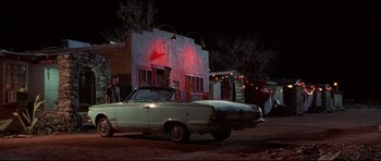 Movie still from “3000 Miles to Graceland” (2001), directed by Demian Lichtenstein – A man standing next to a car in front of a building; Wide shot, Low angle