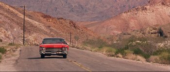 Movie still from “3000 Miles to Graceland” (2001), directed by Demian Lichtenstein – A red car is driving down the street; Extreme Wide shot, Low angle