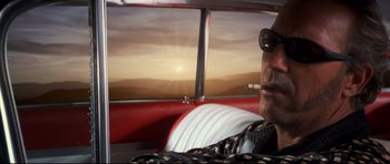 Movie still from “3000 Miles to Graceland” (2001), directed by Demian Lichtenstein – A man sitting in the back seat of a red car; Close Up shot, Low angle