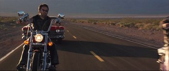 Movie still from “3000 Miles to Graceland” (2001), directed by Demian Lichtenstein – A man riding on the back of a motorcycle down the middle of a road; Wide shot, Low angle