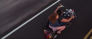 Movie still from “3000 Miles to Graceland” (2001), directed by Demian Lichtenstein – A man and a woman riding a motorcycle down a street; Wide shot, Overhead angle
