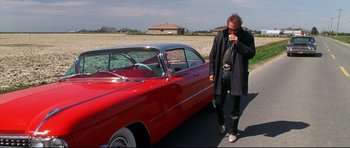 Movie still from “3000 Miles to Graceland” (2001), directed by Demian Lichtenstein – A man standing in front of a red classic car; Wide shot, Low angle