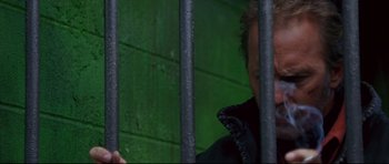 Movie still from “3000 Miles to Graceland” (2001), directed by Demian Lichtenstein – A man behind a metal fence looking out at a green wall; Close Up shot, Low angle