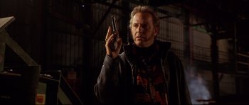 Movie still from “3000 Miles to Graceland” (2001), directed by Demian Lichtenstein – A man holding a gun while standing next to a building; Close Up shot, Low angle