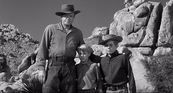 Movie still from “3:10 to Yuma” (1957), directed by Delmer Daves – An older man and two young boys standing next to each other in front of a rock formation; Medium shot, Low angle