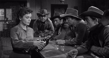 Movie still from “3:10 to Yuma” (1957), directed by Delmer Daves – A group of people sitting around a table with a bottle; Medium shot, Over the shoulder angle