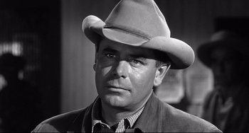 Movie still from “3:10 to Yuma” (1957), directed by Delmer Daves – A man wearing a cowboy hat in a black and white photo; Close Up shot, Over the shoulder angle