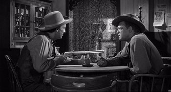 Movie still from “3:10 to Yuma” (1957), directed by Delmer Daves – Two men sitting at a table with guns in their hands; Medium shot, Over the shoulder angle