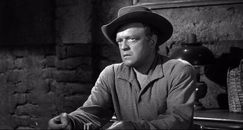 Movie still from “3:10 to Yuma” (1957), directed by Delmer Daves – A man wearing a cowboy hat sitting in front of a brick wall; Close Up shot, Low angle