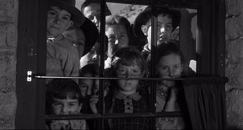 Movie still from “3:10 to Yuma” (1957), directed by Delmer Daves – A black and white photo of a group of children looking out a window; Medium shot, High angle