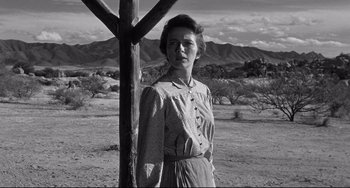 Movie still from “3:10 to Yuma” (1957), directed by Delmer Daves – A woman standing next to a wooden pole in the desert; Medium shot, Low angle
