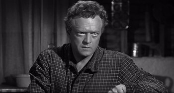 Movie still from “3:10 to Yuma” (1957), directed by Delmer Daves – A man in a black and white photo with his arms crossed; Close Up shot, Over the shoulder angle