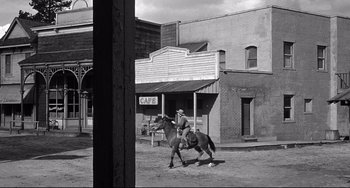 Movie still from “3:10 to Yuma” (1957), directed by Delmer Daves – A man riding a horse down a street; Wide shot, Over the shoulder angle