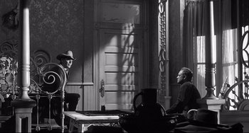 Movie still from “3:10 to Yuma” (1957), directed by Delmer Daves – Two men sitting at a table in a room; Wide shot, Over the shoulder angle