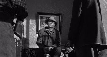 Movie still from “3:10 to Yuma” (1957), directed by Delmer Daves – An older man sitting on a couch in a living room; Medium shot, Over the shoulder angle