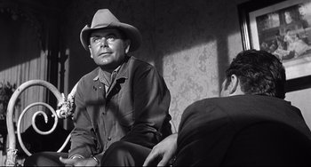 Movie still from “3:10 to Yuma” (1957), directed by Delmer Daves – A man wearing a cowboy hat sitting next to another man; Medium shot, Over the shoulder angle