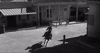 Movie still from “3:10 to Yuma” (1957), directed by Delmer Daves – A man riding a horse down the middle of a street; Extreme Wide shot, High angle