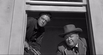 Movie still from “3:10 to Yuma” (1957), directed by Delmer Daves – A man and an older man are looking out of a window; Medium shot, Low angle