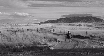 Movie still from “3:10 to Yuma” (1957), directed by Delmer Daves – A man riding a horse and buggy down a dirt road; Extreme Wide shot, Over the shoulder angle