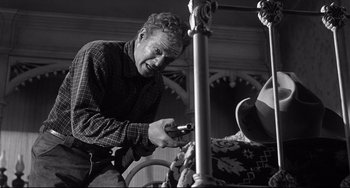 Movie still from “3:10 to Yuma” (1957), directed by Delmer Daves – An older man working on an object in a black and white photo; Medium shot, Low angle