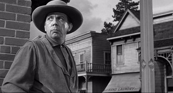 Movie still from “3:10 to Yuma” (1957), directed by Delmer Daves – A man wearing a hat standing in front of a building; Medium shot, Low angle