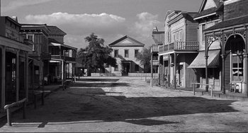 Movie still from “3:10 to Yuma” (1957), directed by Delmer Daves – An old western town with buildings and a tree in black and white; Extreme Wide shot, High angle
