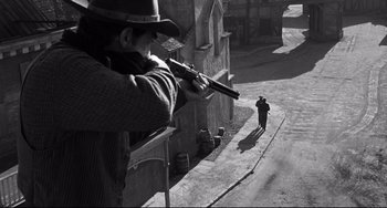 Movie still from “3:10 to Yuma” (1957), directed by Delmer Daves – A man with a gun and a man walking down a street; Wide shot, Over the shoulder angle