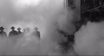 Movie still from “3:10 to Yuma” (1957), directed by Delmer Daves – A group of men standing next to each other in the smoke; Wide shot, Low angle