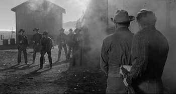 Movie still from “3:10 to Yuma” (1957), directed by Delmer Daves – A black and white photo of a group of men standing in front of a building; Wide shot, Over the shoulder angle
