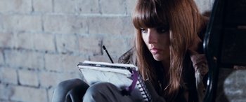 Movie still from “4.3.2.1.” (2010), directed by Mark Davis – A woman sitting in front of a brick wall writing on a notebook; Close Up shot, High angle