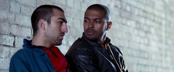 Movie still from “4.3.2.1.” (2010), directed by Mark Davis – Two men are standing next to a brick wall; Close Up shot, Over the shoulder angle