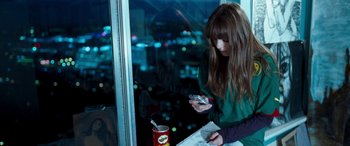 Movie still from “4.3.2.1.” (2010), directed by Mark Davis – A woman is looking at her cell phone while sitting in front of a window; Medium shot, High angle
