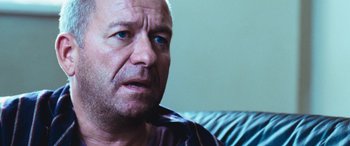 Movie still from “4.3.2.1.” (2010), directed by Mark Davis – A person sitting on a couch looking at the camera; Close Up shot, Over the shoulder angle