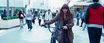 Movie still from “4.3.2.1.” (2010), directed by Mark Davis – A woman is riding a bike down the street; Medium shot, Over the shoulder angle