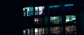 Movie still from “4.3.2.1.” (2010), directed by Mark Davis – People are standing in a building lit up at night; Extreme Wide shot, Low angle