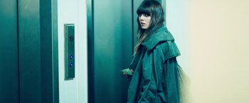 Movie still from “4.3.2.1.” (2010), directed by Mark Davis – A woman standing in front of an elevator holding a cell phone; Medium shot, Over the shoulder angle