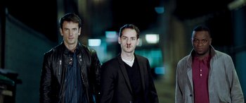 Movie still from “4.3.2.1.” (2010), directed by Mark Davis – Two men standing next to each other on a street at night; Medium shot, Low angle