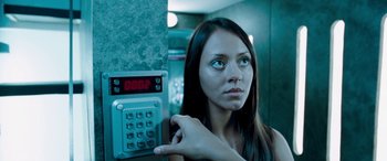 Movie still from “4.3.2.1.” (2010), directed by Mark Davis – A woman is looking at the camera while holding her hand on a button; Close Up shot, Low angle