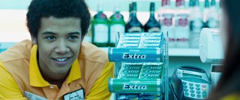 Movie still from “4.3.2.1.” (2010), directed by Mark Davis – A man in an orange and yellow shirt is behind a display of cans of soda; Close Up shot, Over the shoulder angle