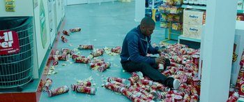 Movie still from “4.3.2.1.” (2010), directed by Mark Davis – A man sitting on the floor with a lot of cans; Wide shot, High angle