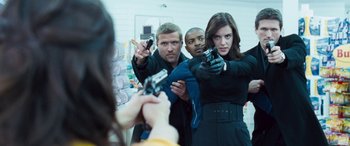 Movie still from “4.3.2.1.” (2010), directed by Mark Davis – A group of men and women holding guns in a room; Medium shot, Over the shoulder angle