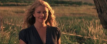 A beautiful blonde woman standing in front of a field