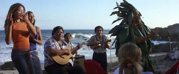 Movie still from “50 First Dates” (2004), directed by Peter Segal – A group of people playing music on the beach; Wide shot, Over the shoulder angle