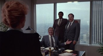 Movie still from “52 Pick-Up” (1986), directed by John Frankenheimer – A group of men standing in front of a window in an office; Wide shot, Over the shoulder angle