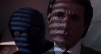 Movie still from “52 Pick-Up” (1986), directed by John Frankenheimer – A person wearing a suit and a mask; Close Up shot, Over the shoulder angle