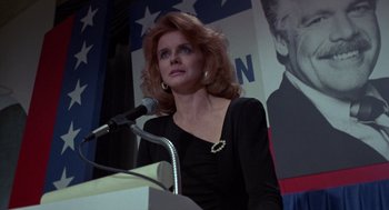 Movie still from “52 Pick-Up” (1986), directed by John Frankenheimer – A woman standing at a podium in front of a microphone; Close Up shot, Low angle