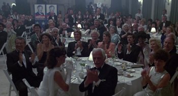 Movie still from “52 Pick-Up” (1986), directed by John Frankenheimer – A group of people sitting at a dinner table clapping; Wide shot, High angle