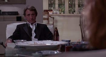 Movie still from “52 Pick-Up” (1986), directed by John Frankenheimer – A man sitting at a dinner table in a suit and tie; Medium shot, Over the shoulder angle